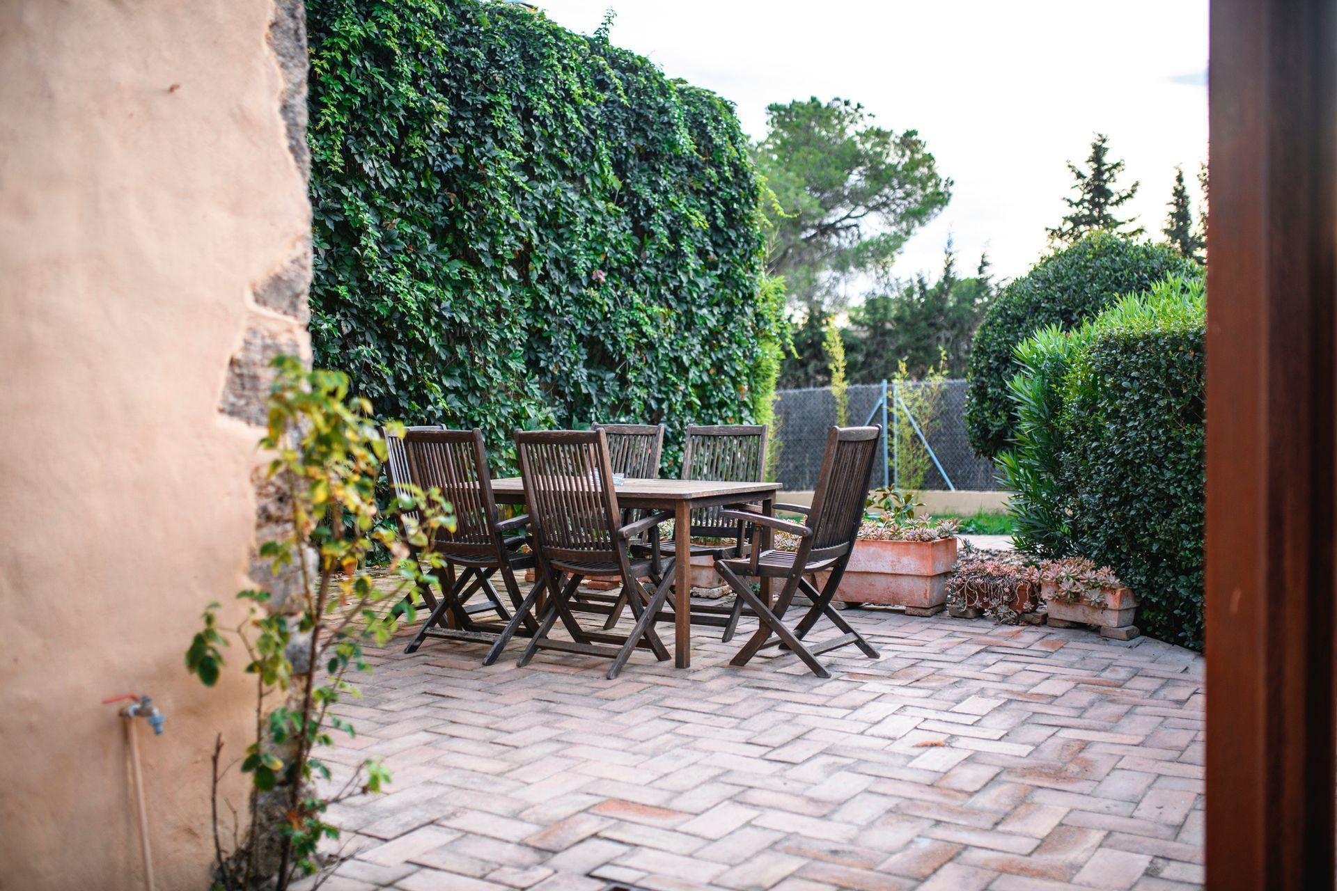 A patio with a table and chairs in front of a hedge.