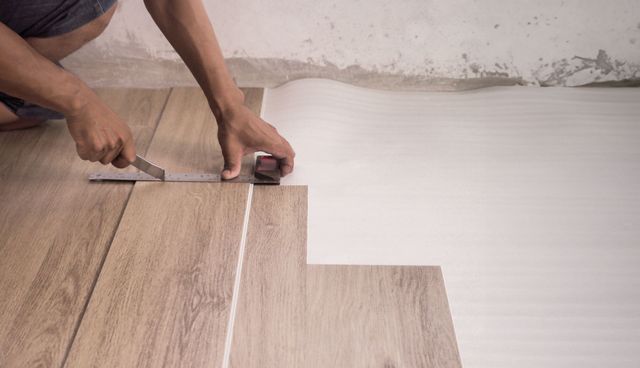 A person is measuring a piece of vinyl flooring with a tape measure.