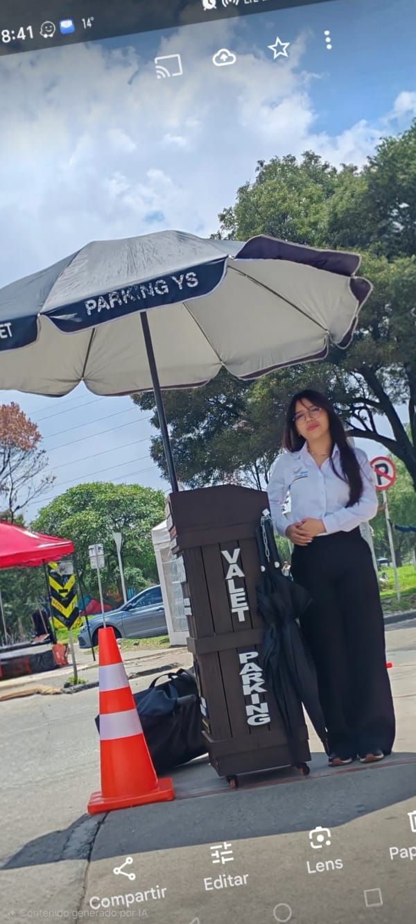 Una persona de pie junto a un cartel exterior bajo una gran sombrilla en un día soleado.