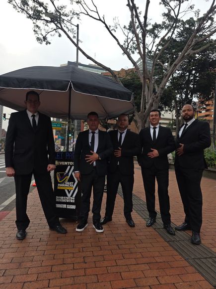 Cinco hombres vestidos con trajes negros  vestidos de valet parking