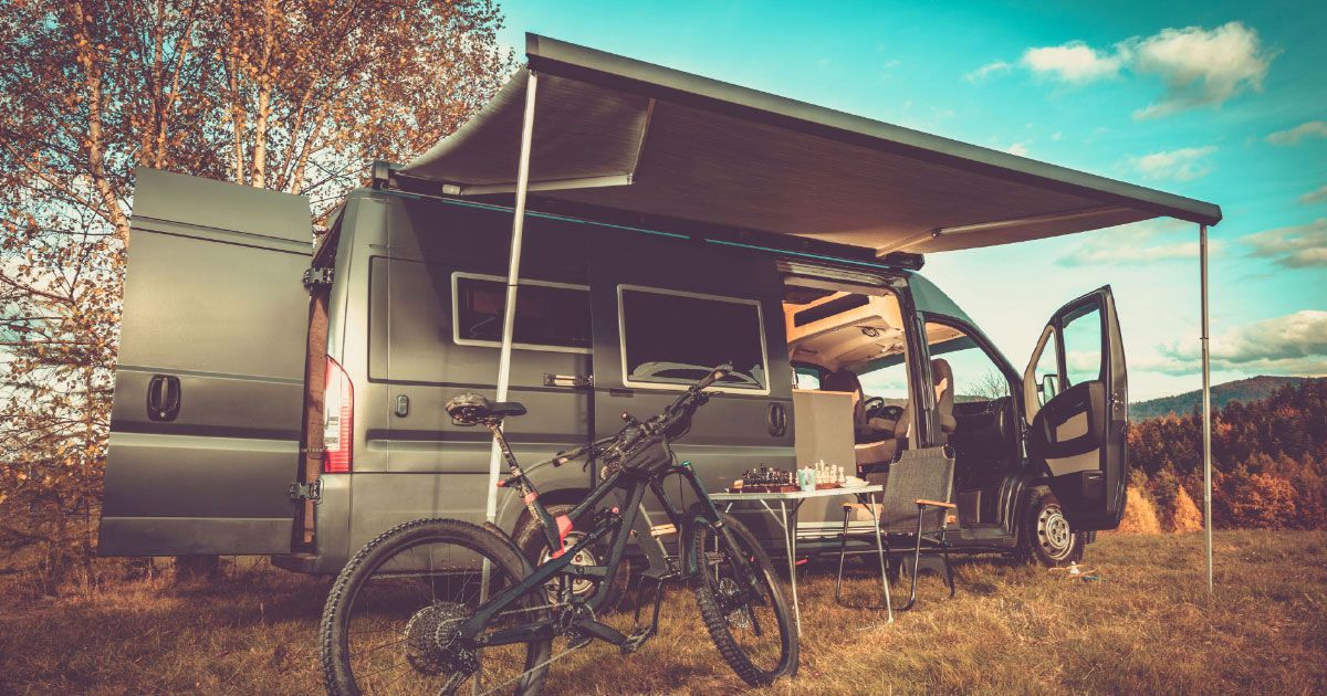 A camper van with an awning and a bicycle parked in front of it.