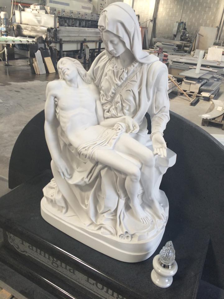 Scultura bianca di Maria che tiene in braccio Gesù morto, su una lapide nera. All'interno, con luci e ombre.