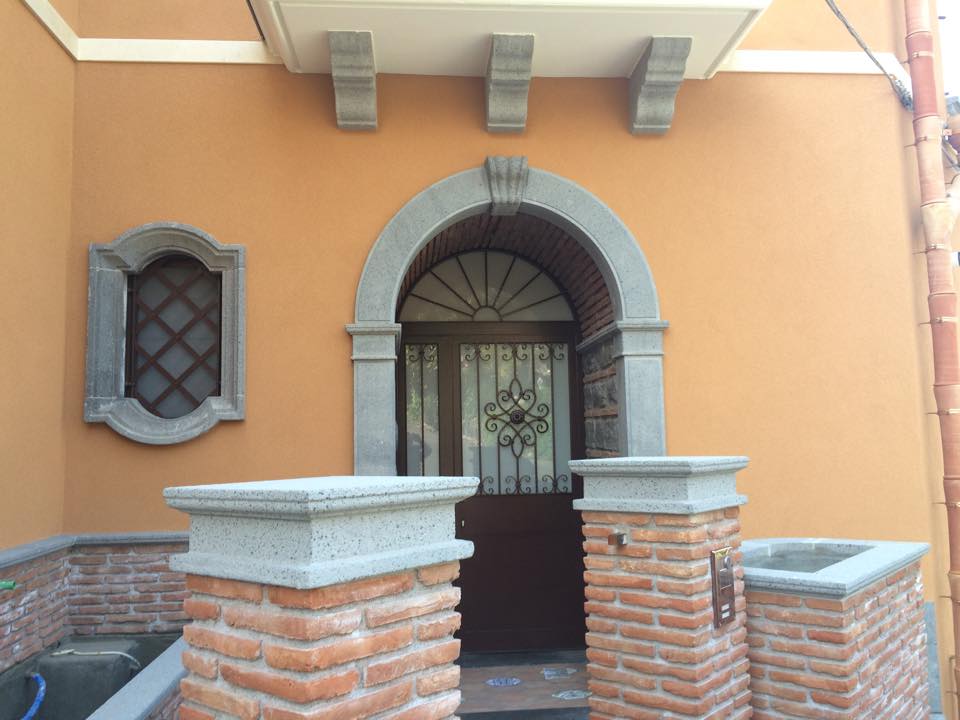 Ingresso dell'edificio in stucco arancione con pilastri in mattoni, porta ad arco e cancello in ferro decorato.