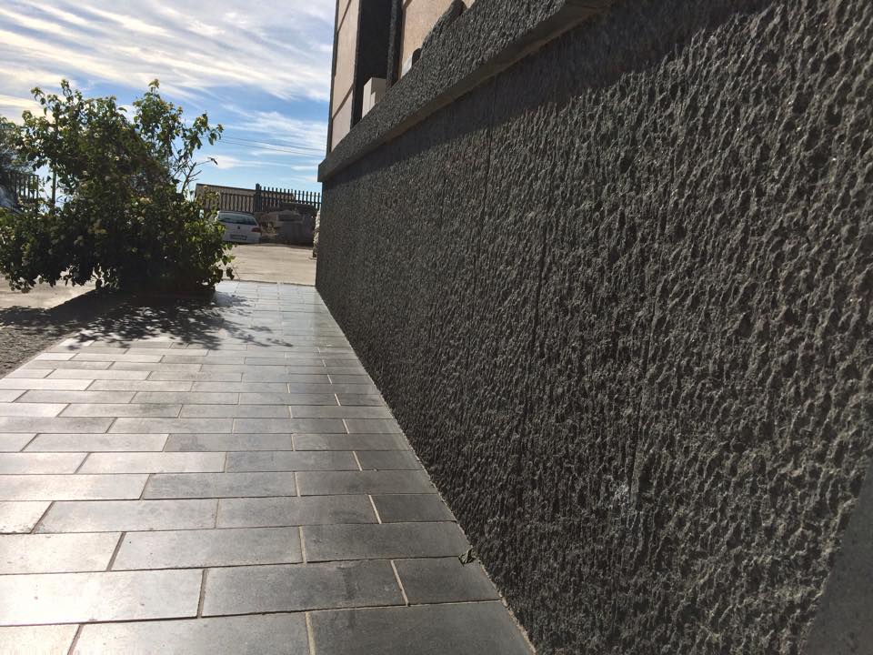 Esterno di un edificio dalla texture grigia con passerella in mattoni e cielo coperto.