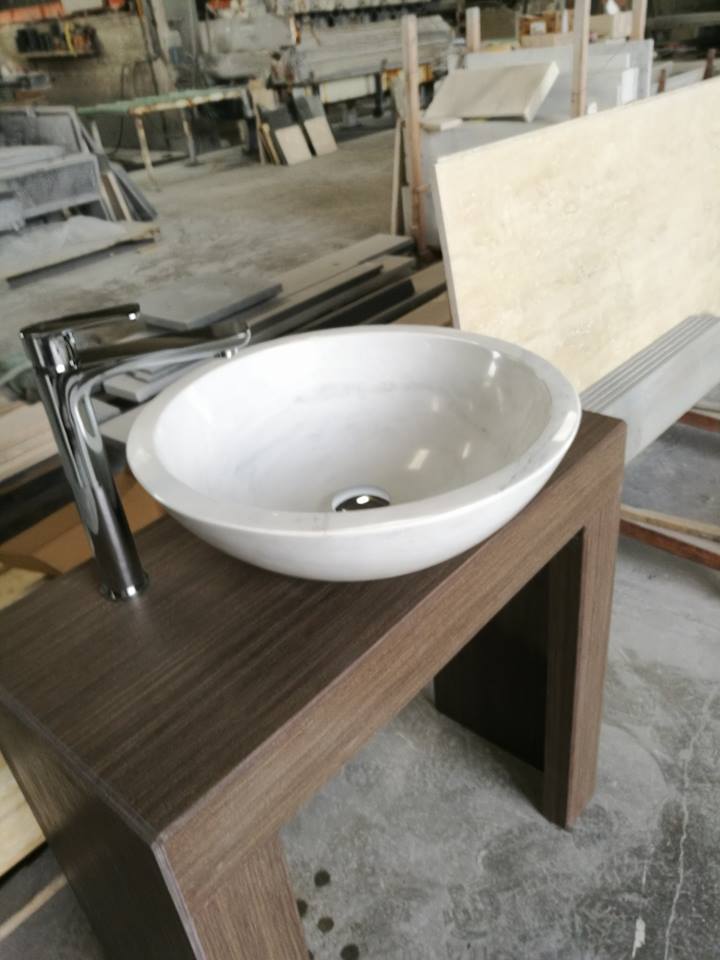Lavandino ovale bianco con rubinetto cromato su un mobile in legno marrone in un ambiente da laboratorio.