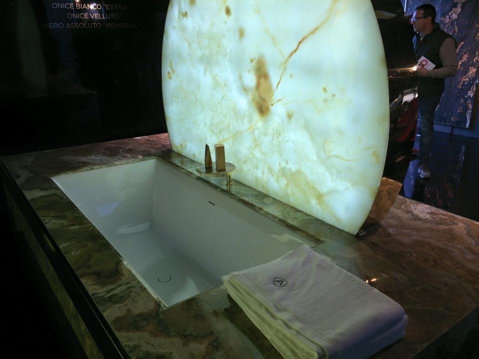 Vasca da bagno con piano in marmo e sfondo in onice luminoso; persona in piedi nelle vicinanze.
