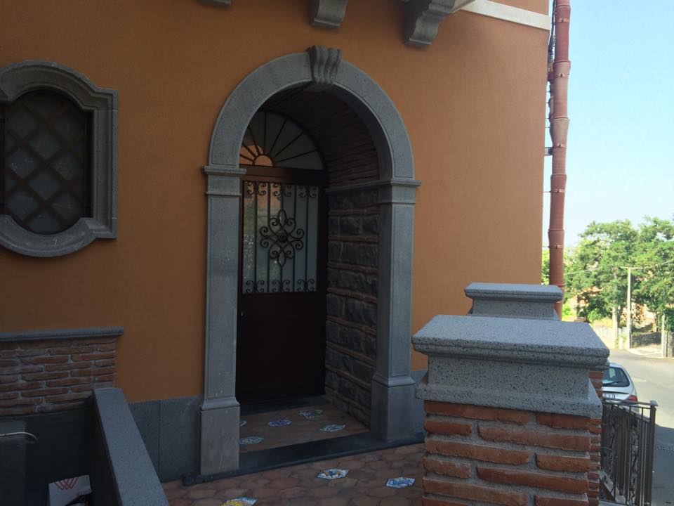 Porta ad arco con cornice in pietra e cancello in ferro, situata in un edificio arancione.