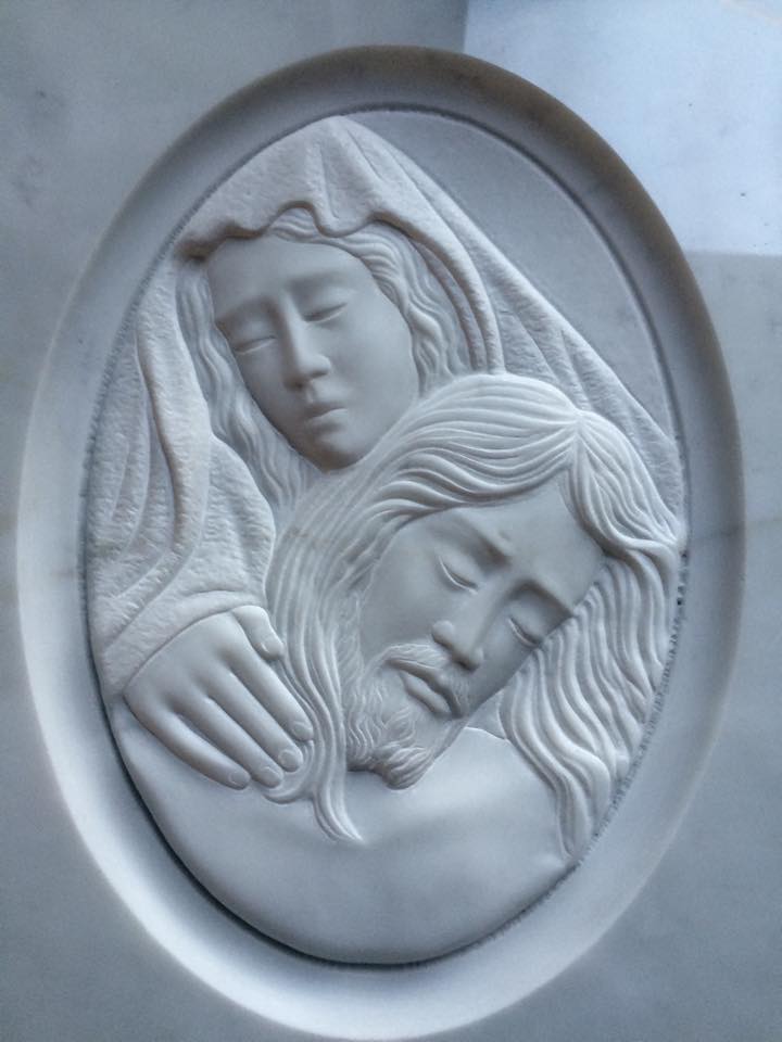 Bassorilievo raffigurante Maria che culla Gesù defunto. Entrambi hanno gli occhi chiusi; bordo ovale.