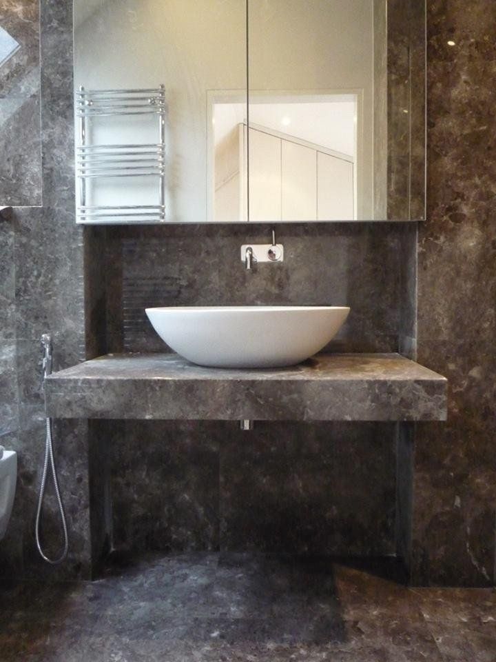 Bagno moderno con piastrelle in marmo scuro, mobile lavabo in pietra galleggiante e lavabo ovale bianco.