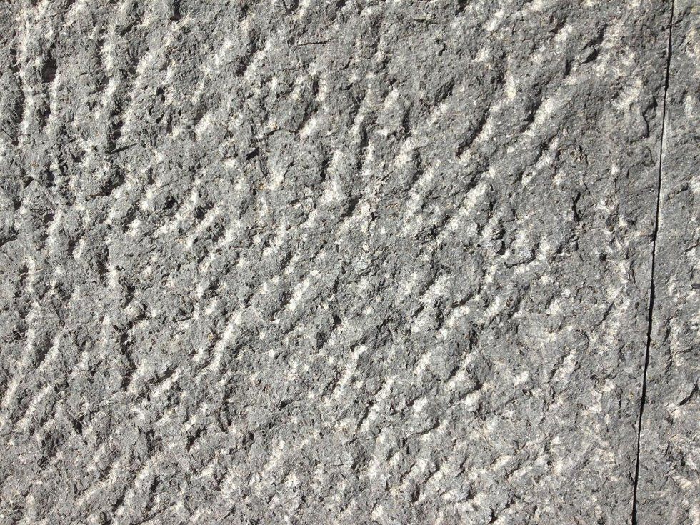 Superficie ruvida in pietra grigia con trama irregolare e motivo diagonale.