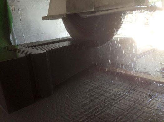 Una grande sega circolare che taglia un blocco di pietra spruzzando acqua.