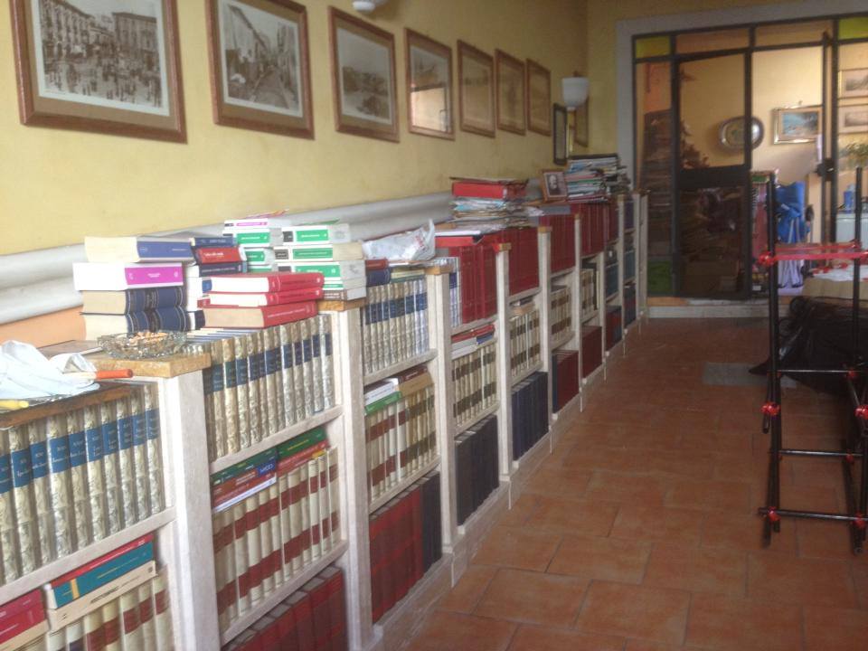 Una parete gialla è ornata da scaffali pieni di libri. Sopra sono appese delle opere d'arte incorniciate.