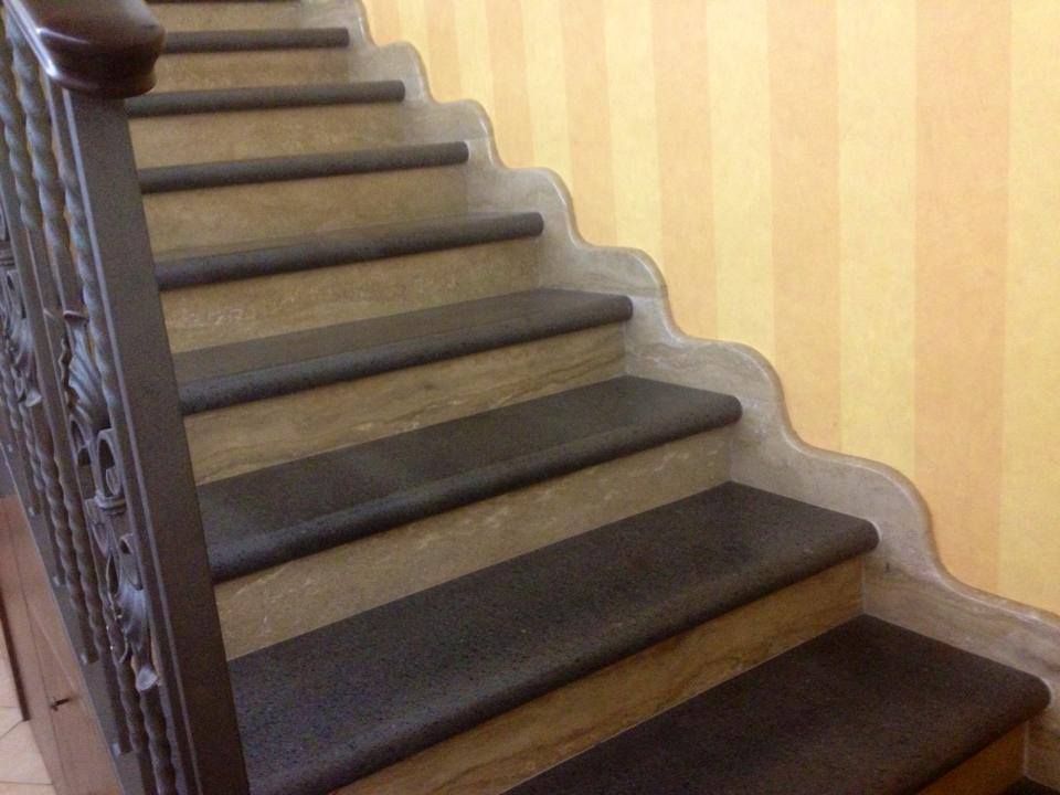 Scala con pedate scure, alzate chiare e parete gialla decorata. Ringhiera in ferro battuto.