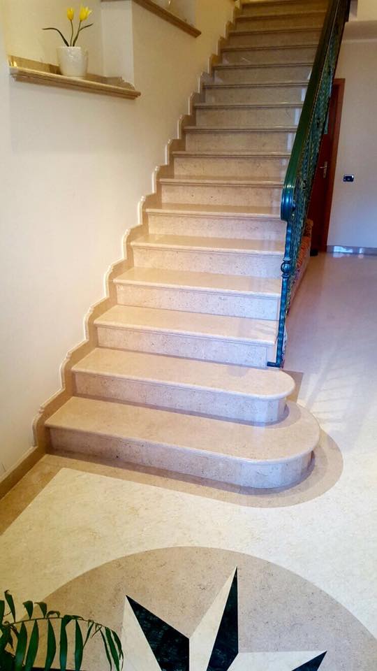 Scala in marmo con bordi curvi, ringhiera decorata e pavimento intarsiato a forma di stella.