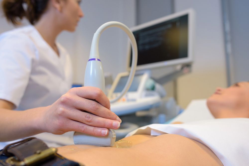 Ecografía a una paciente embarazada mientras un médico sostiene la sonda junto a un monitor.