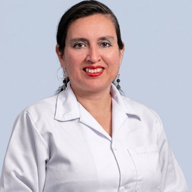 Persona con bata blanca de laboratorio sonriendo sobre un fondo gris claro.