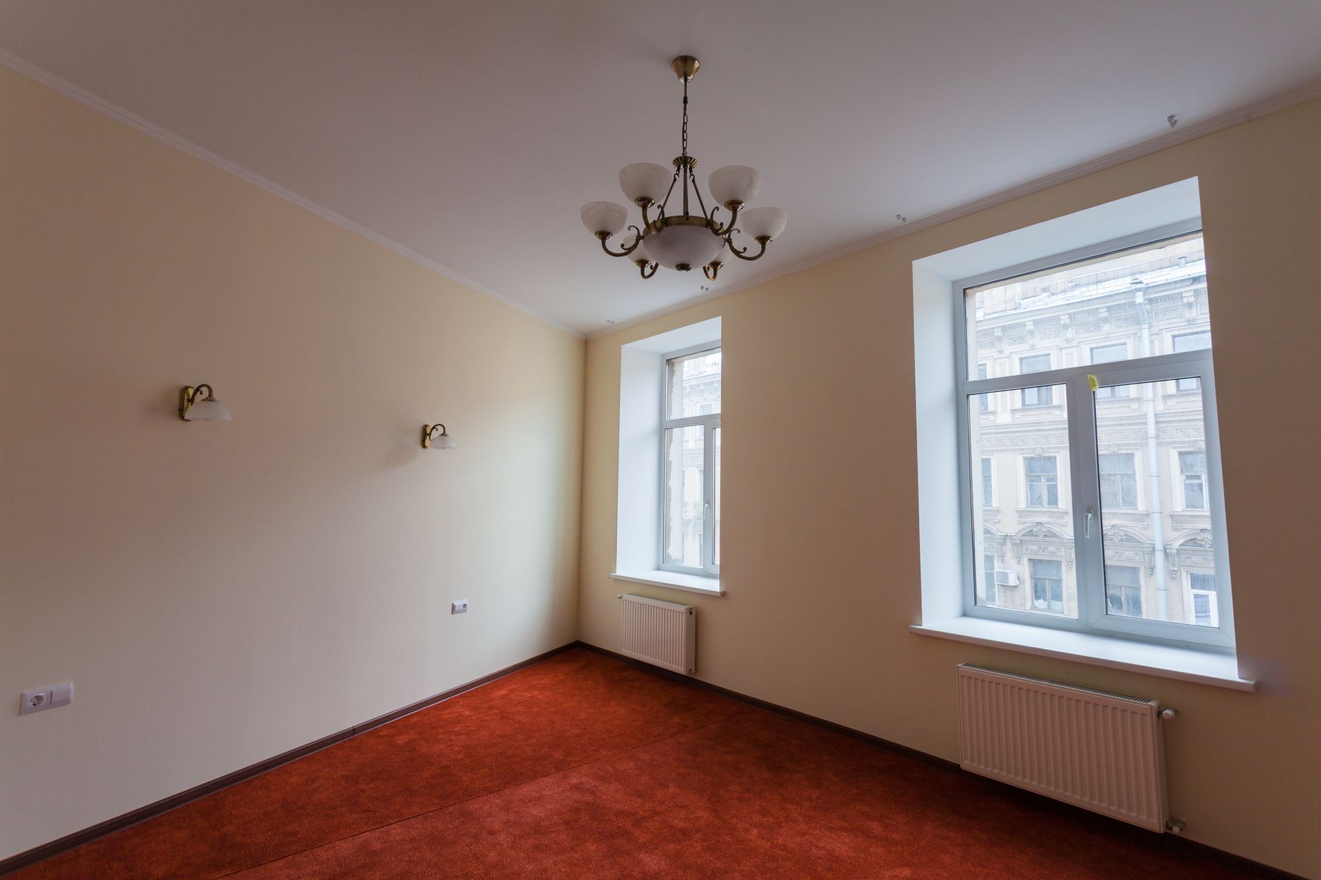 An empty room with a chandelier hanging from the ceiling and two windows.