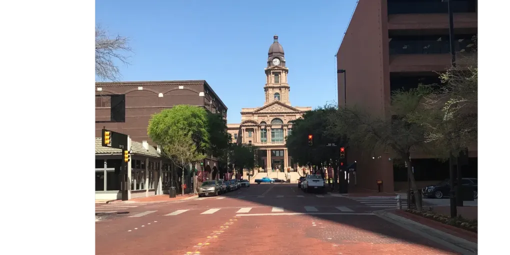 Street view of a brick road leading to a tall building with a clock tower under a clear sky.