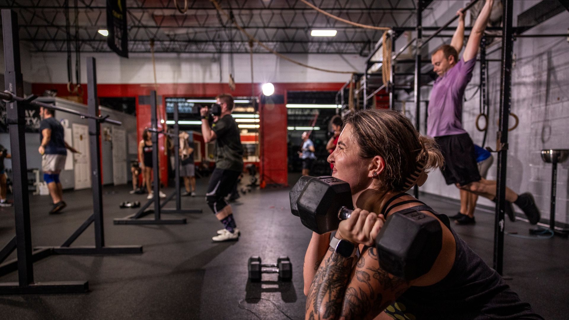 Woman squats with dumbbells doing a CrossFit workout in Winter Park, FL. Others exercise with pull-ups and weights.