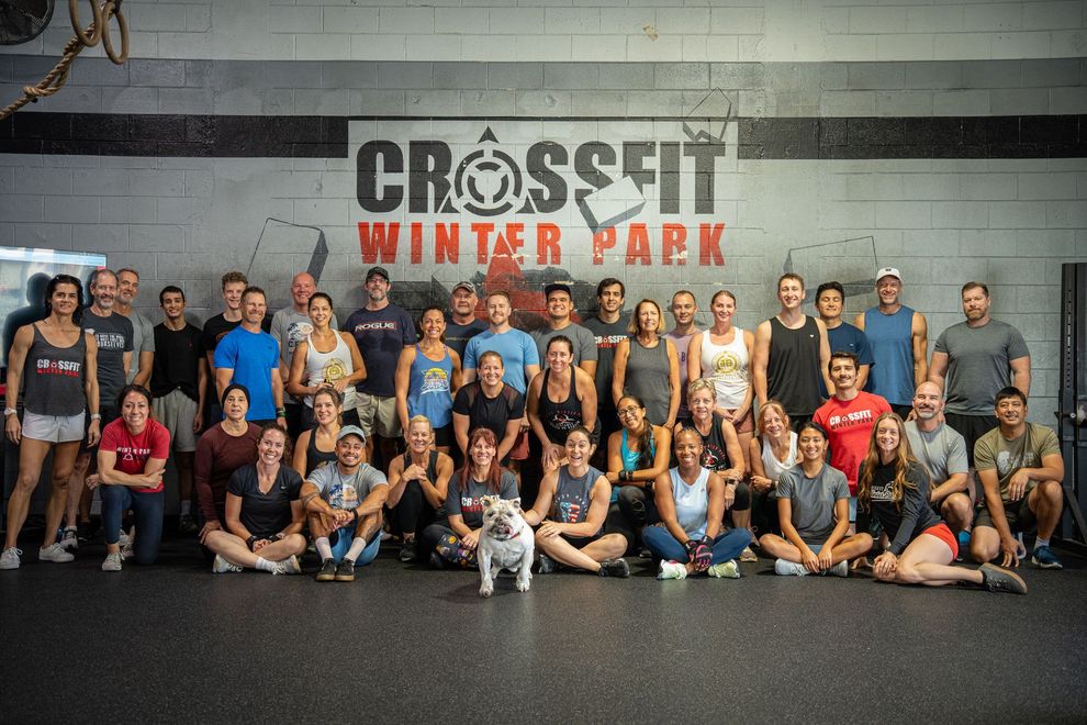 Group photo at CrossFit Winter Park. People of various sizes and attire pose in front of a wall with the gym's logo