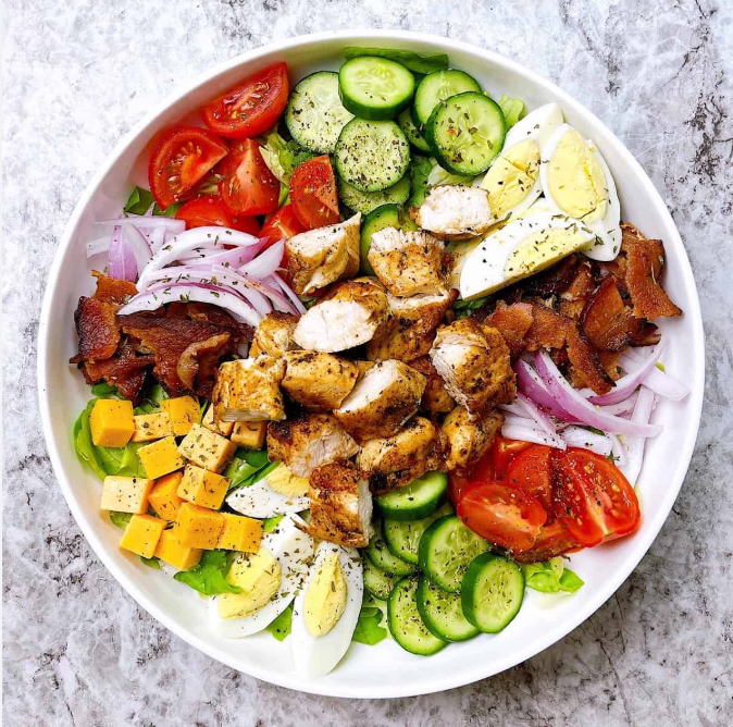 Salad with tomatoes, cucumber, chicken, bacon, eggs, onion, and cheese.