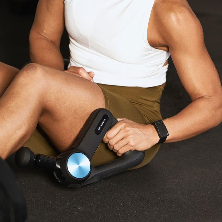 Person using a massage gun on their thigh while sitting.