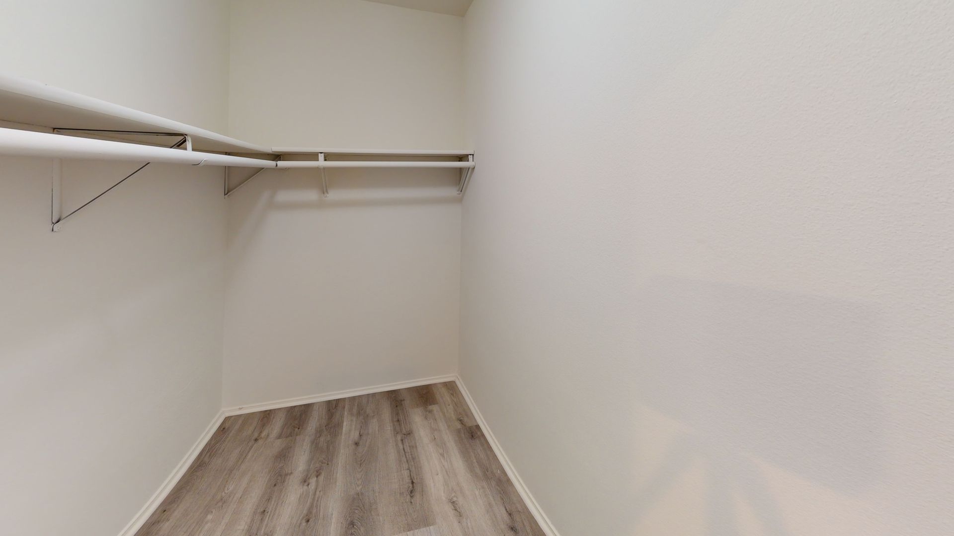 Empty closet with white walls, shelves, and gray wood-look flooring.