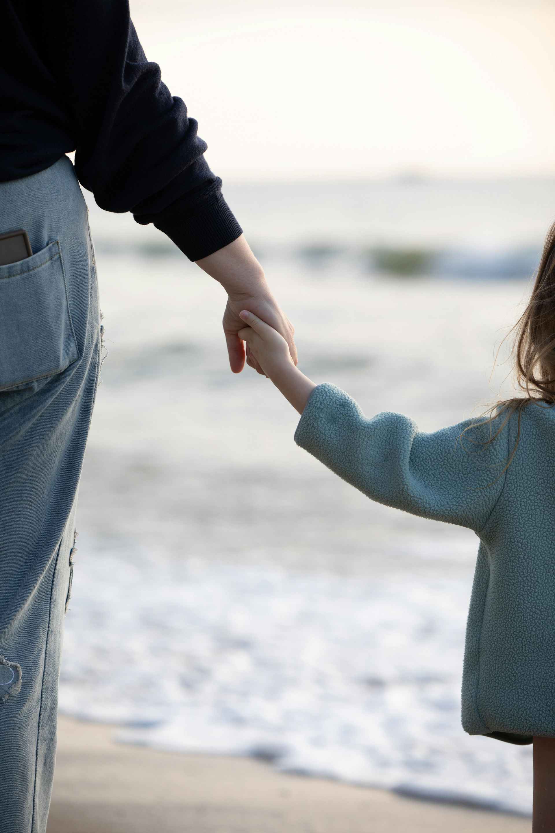 Adult and child holding hands on a beach, with the ocean in the background