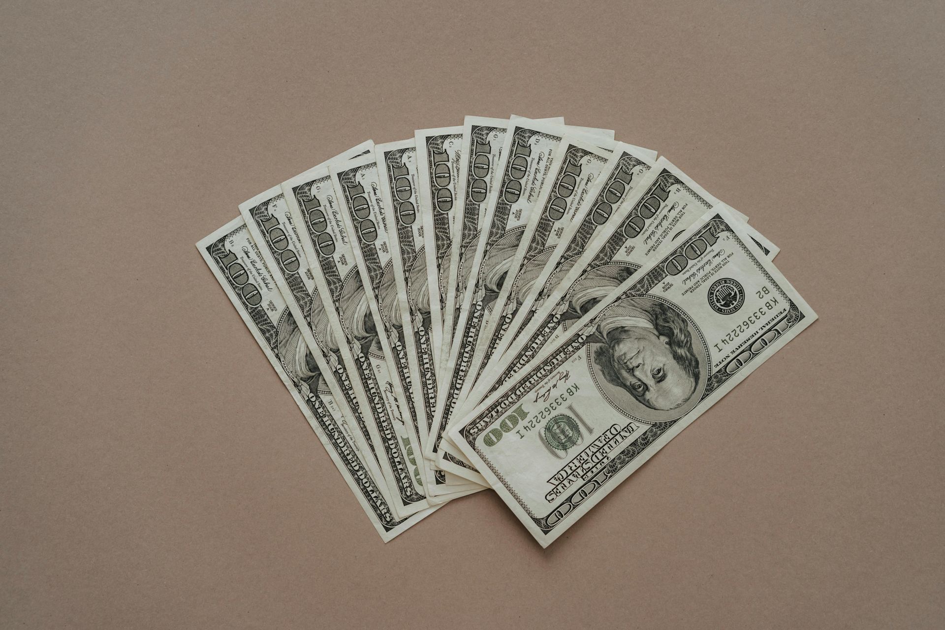 A fan of US hundred-dollar bills on a light brown surface.