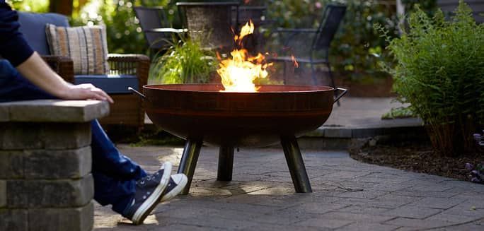 A person is sitting next to a fire pit with a duraflame fire burning