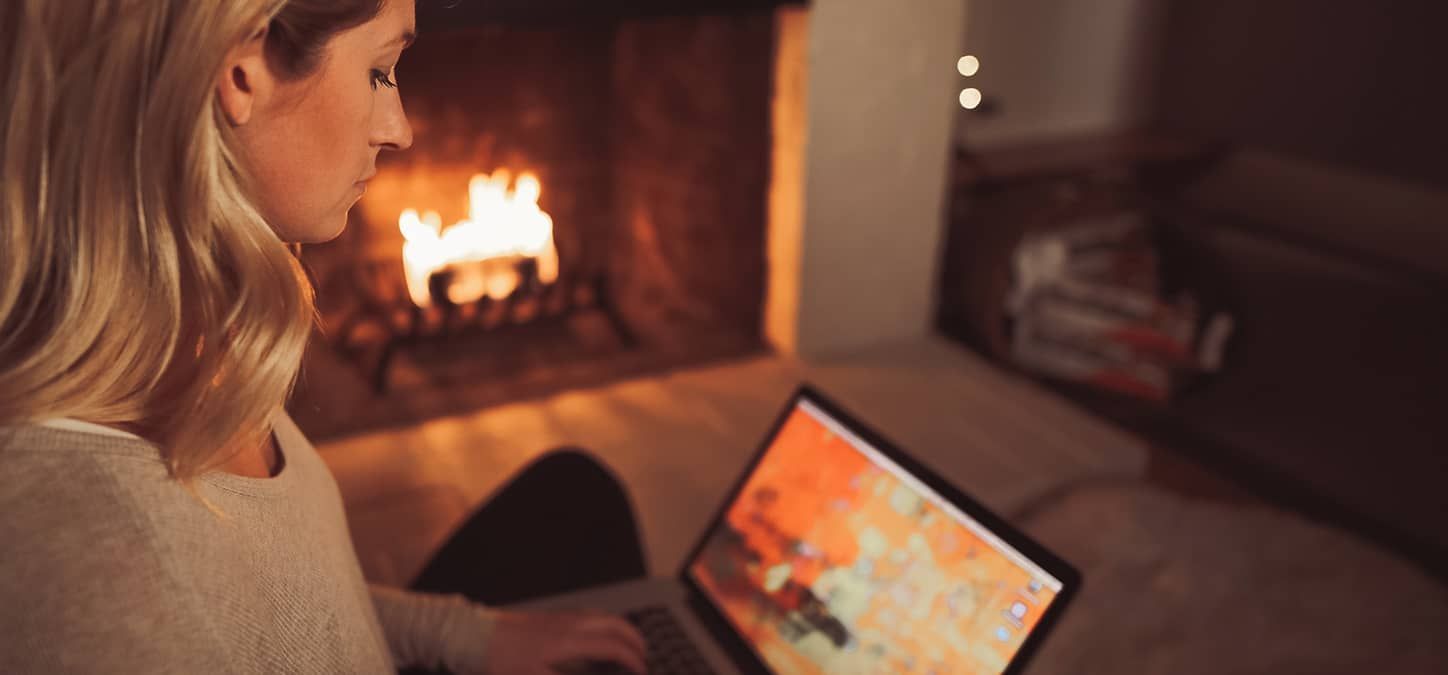 A woman is sitting in front of a fireplace using a laptop computer.