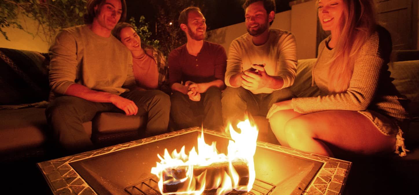 A group of people are sitting around a fire pit with a duraflame firelog burning