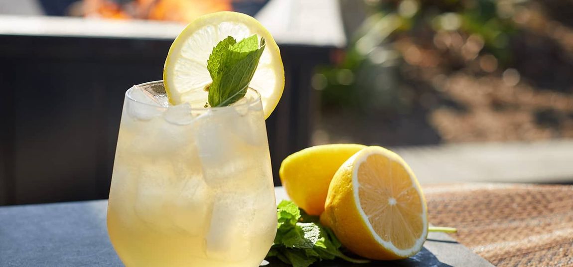 Iced citrus drink with lemon garnish on a table beside sliced lemons and mint
