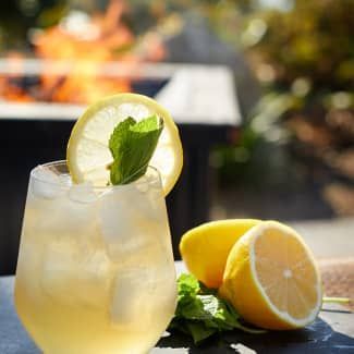 Lemon cocktail in a glass with mint and lemon slices beside halved lemons on a table