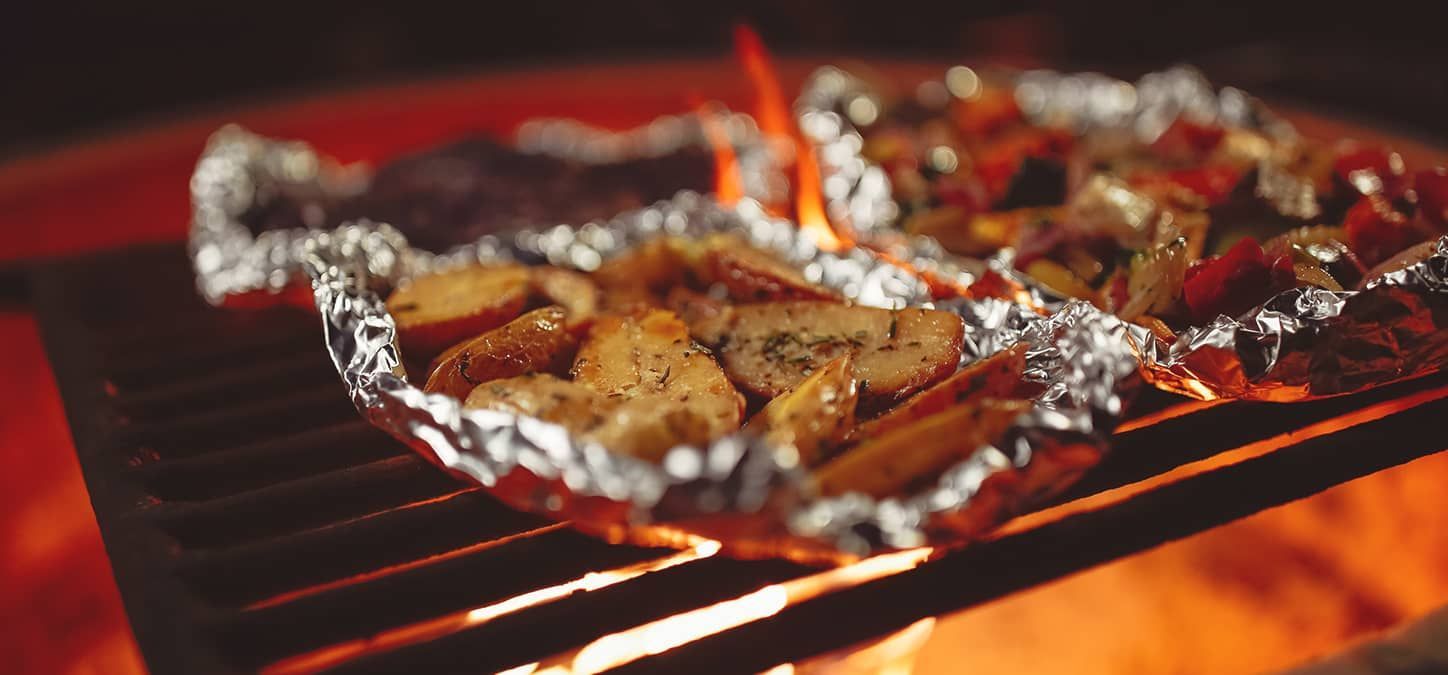 A foil packet of balsamic grilled vegetables is cooking over a campfire.