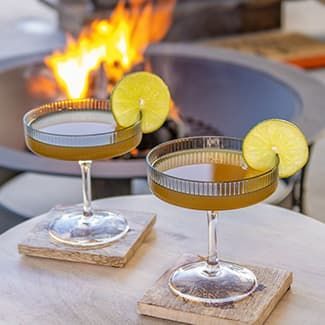 Two boondock cocktails with lime garnish on a patio table beside a fire pit