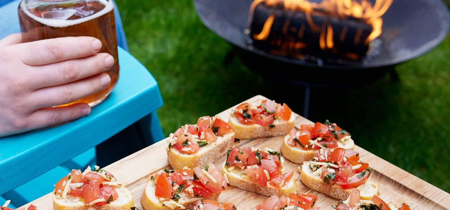 A cutting board filled with bruschette is in front of a fire pit