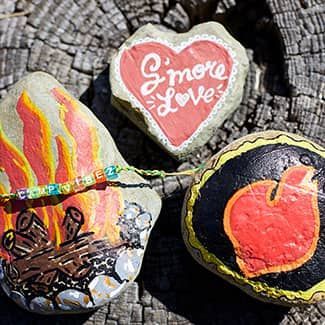 Three painted rocks are sitting on top of a tree stump.