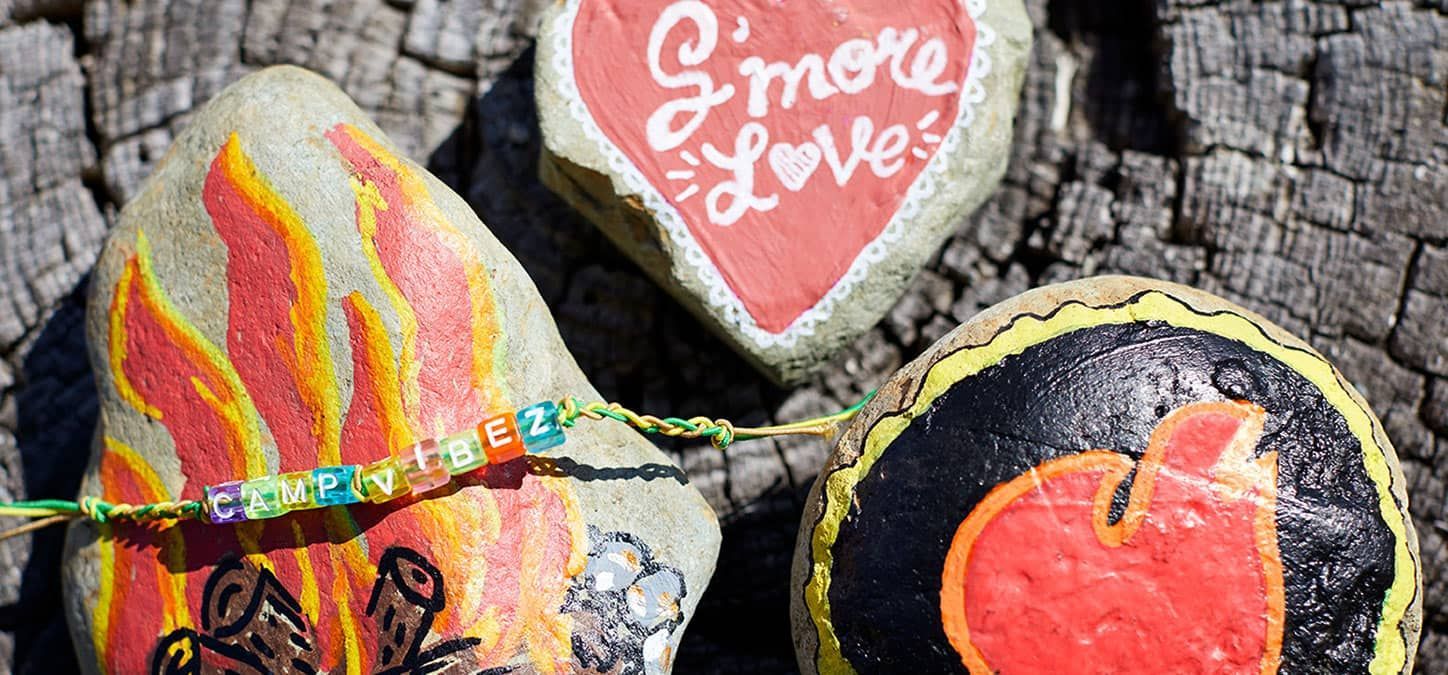 Three painted rocks are sitting on a tree trunk.
