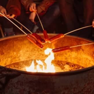 Hot dogs roasting over a campfire.