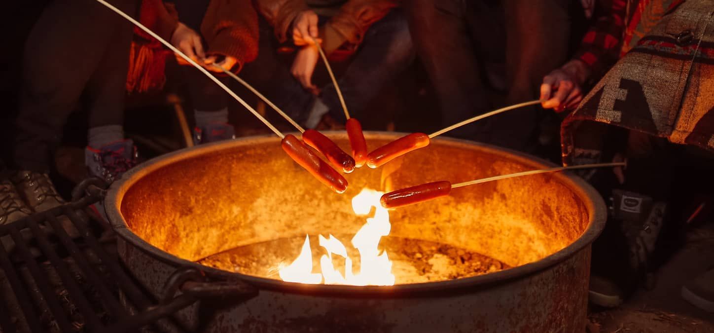 A group of people are roasting hot dogs over a fire pit.