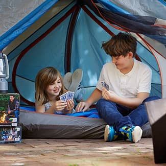 A boy and a girl are playing cards in a tent.