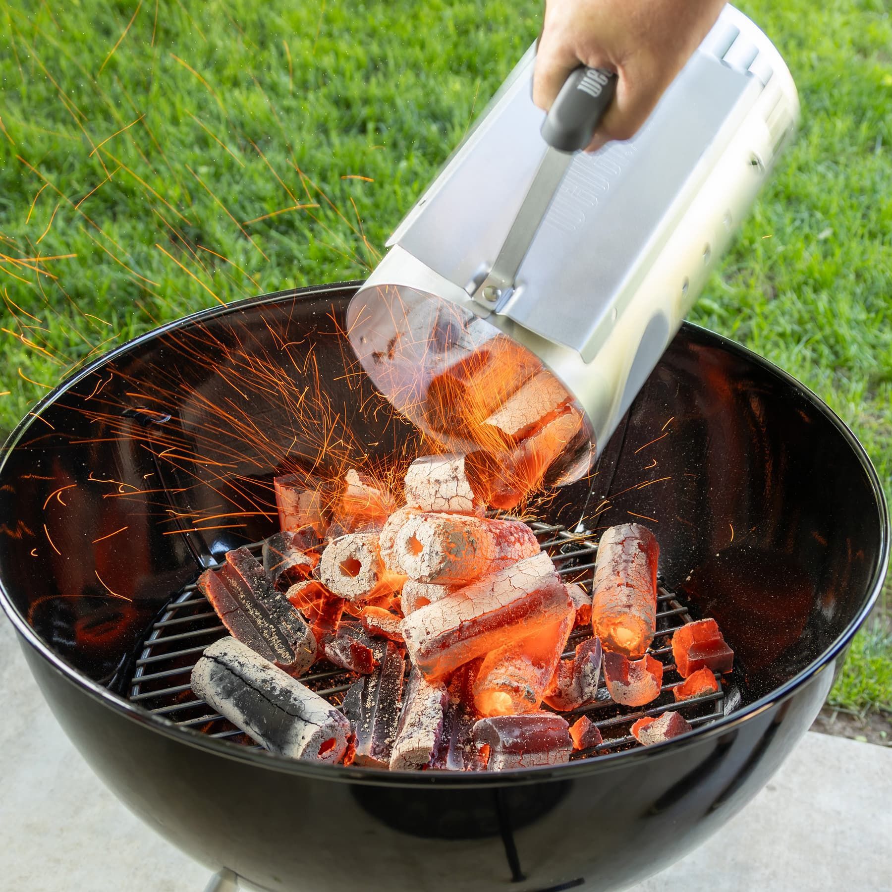 Charcoal grill with glowing duraflame char-logs, high quality grilling charcoal logs, being poured from a chimney starter onto the grate of a kettle grill