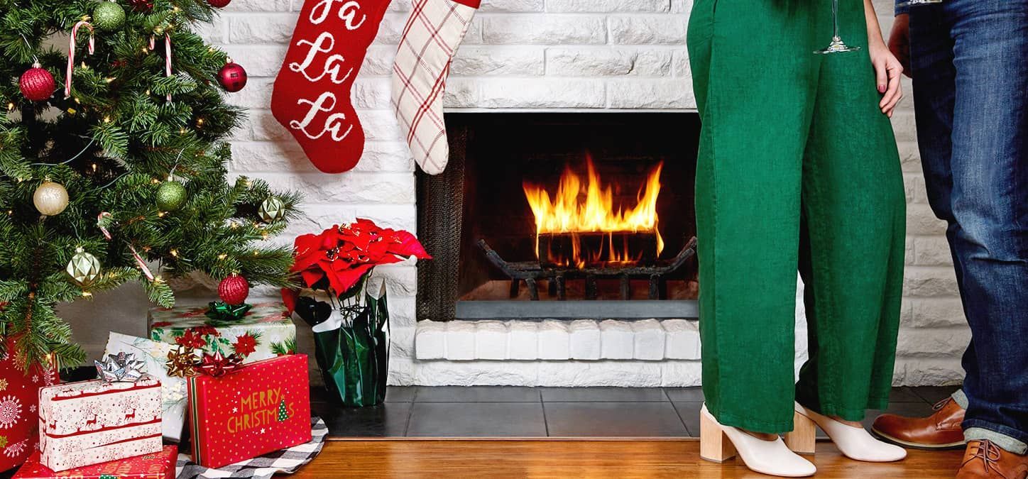 A man and a woman are standing in front of a fireplace and a christmas tree.