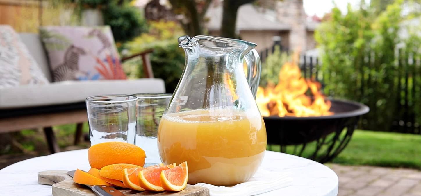 A pitcher of citus sprtiz is sitting on a table next to a fire pit.