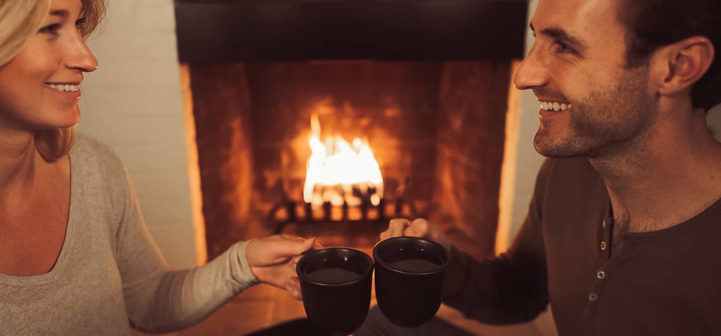 A man and a woman are sitting in front of a fireplace drinking tea.