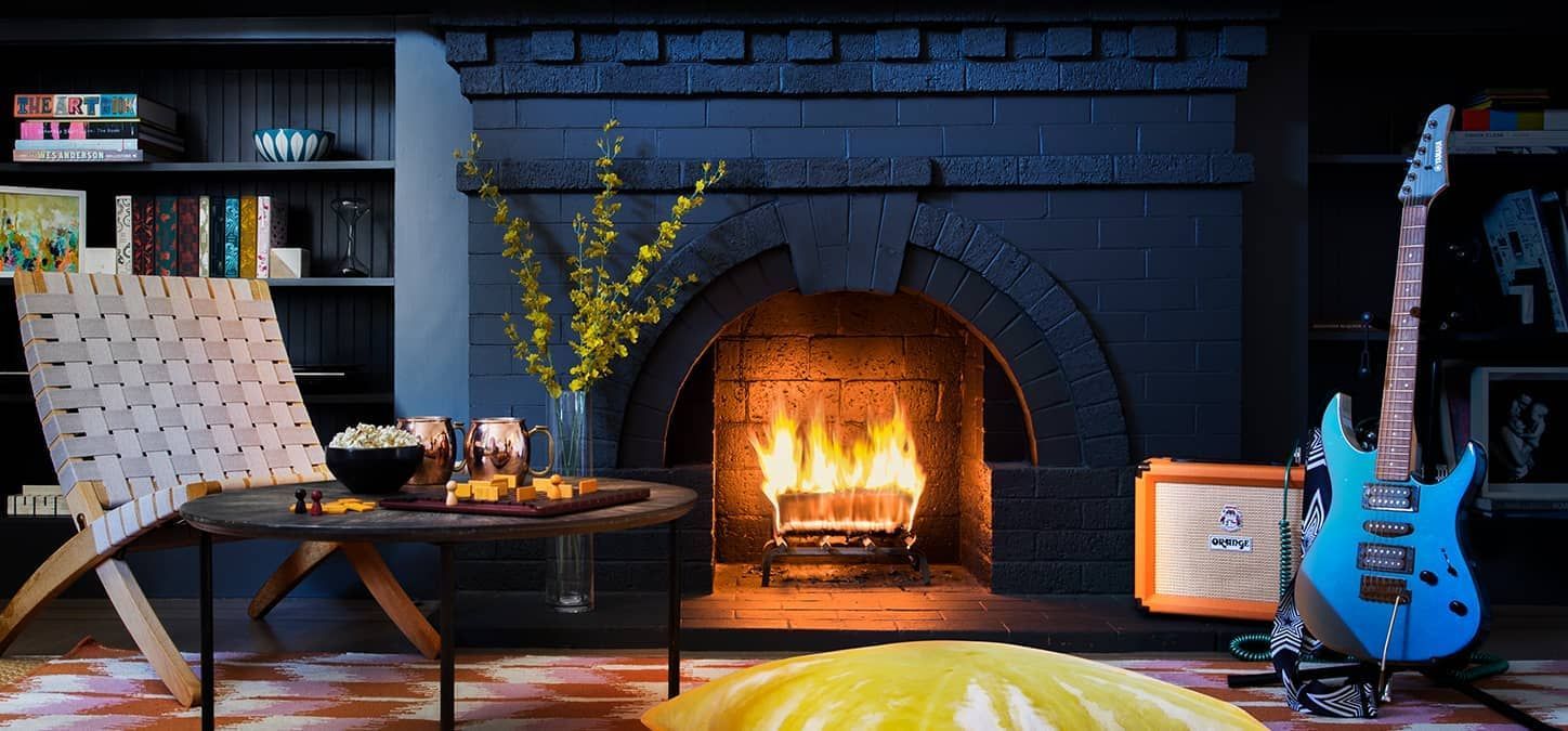 A living room with a duraflame Every Night firelog burning in the fireplace and a blue electric guitar & amp.