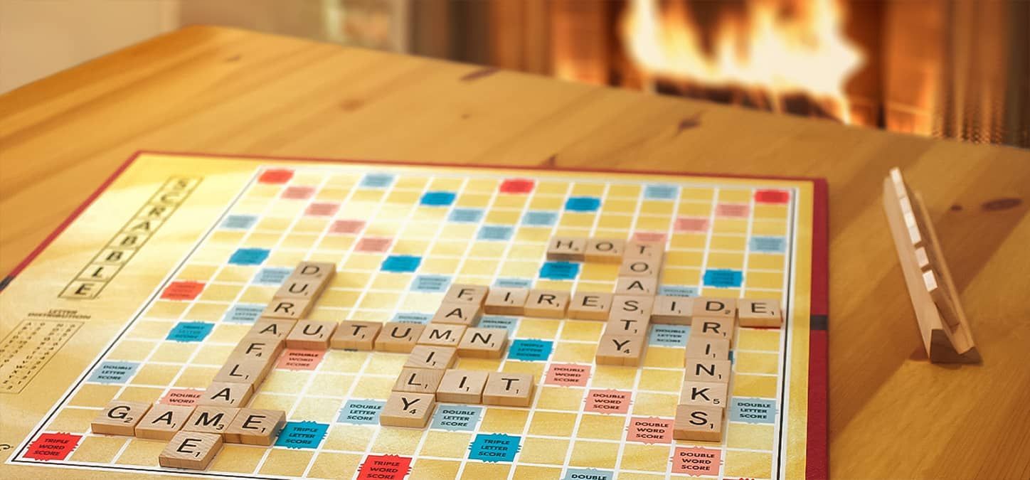 A scrabble game is sitting on a wooden table in front of a fireplace.