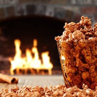 Caramel popcorn in a glass bowl sits on a table, with a fireplace in the background.