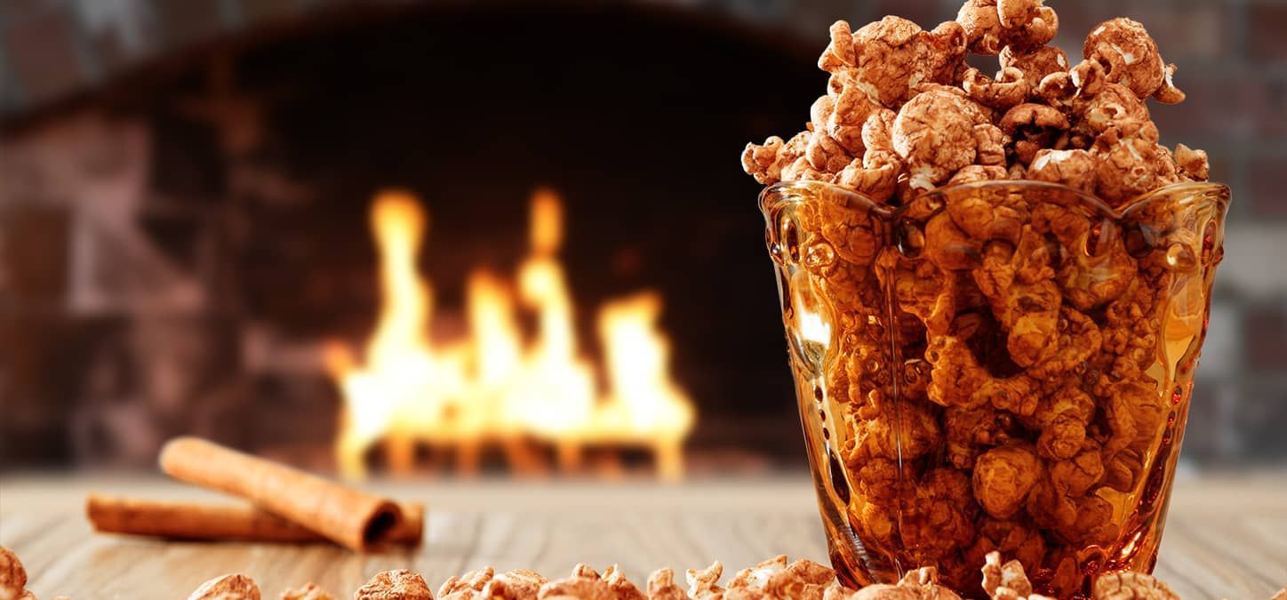 A bowl filled with caramel popcorn is on a table in front of a fireplace.